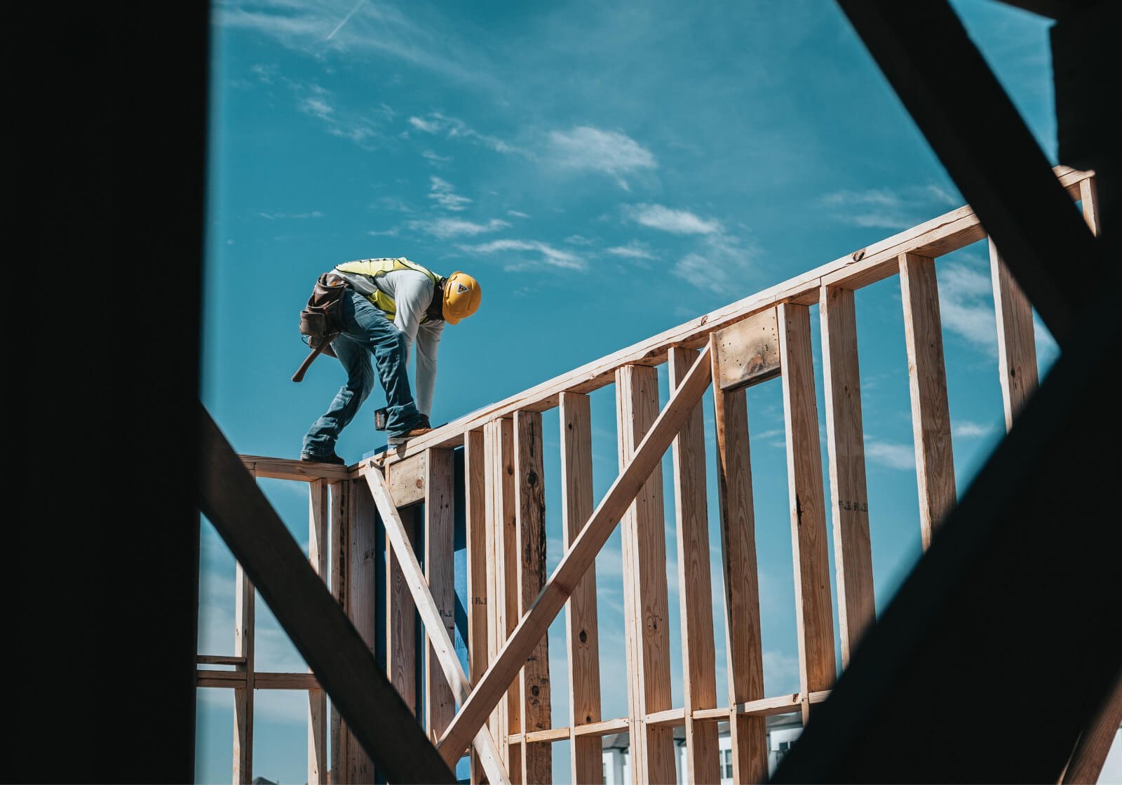 Man walks along wall studs on a construction site.